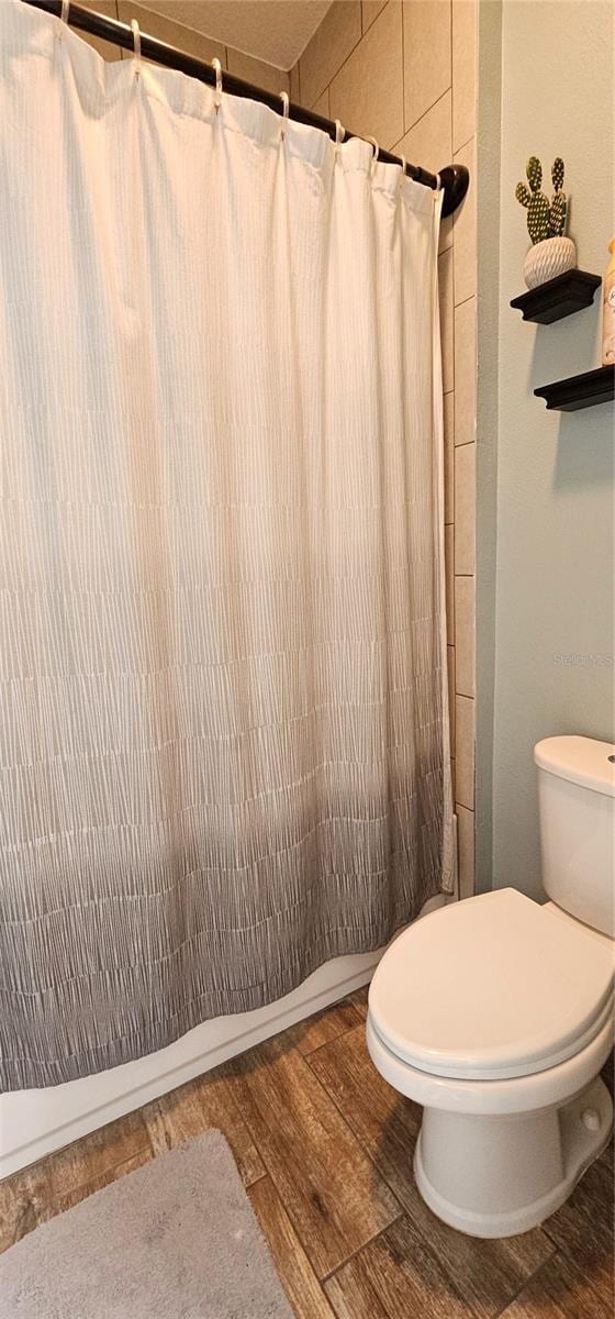 bathroom featuring wood-type flooring, toilet, and a shower with curtain