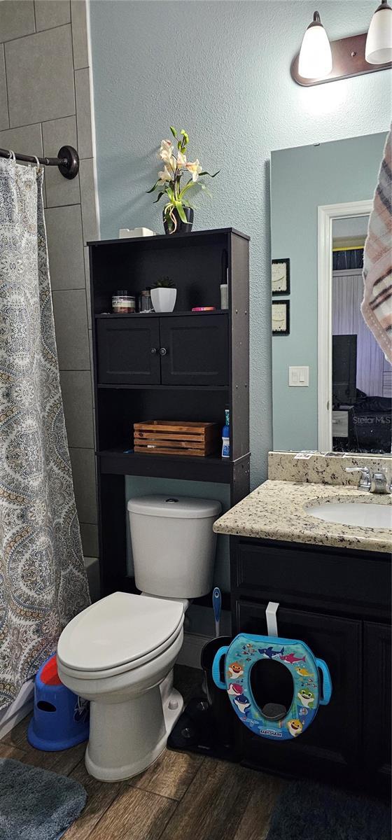 full bathroom with shower / bathtub combination with curtain, vanity, wood-type flooring, and toilet