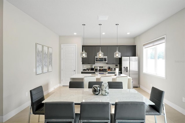 kitchen featuring decorative light fixtures, stainless steel appliances, light tile patterned floors, and a center island with sink