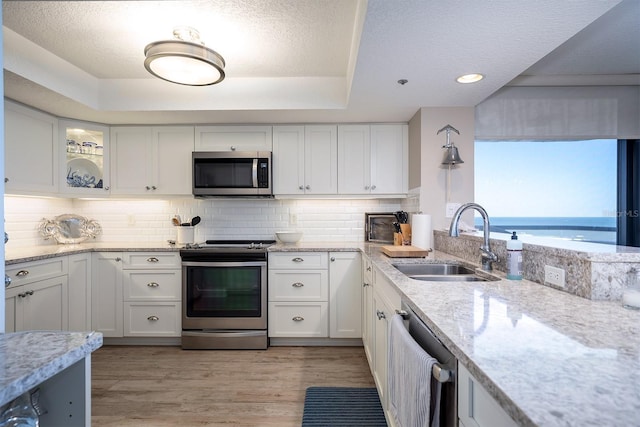 kitchen featuring sink, stainless steel appliances, a water view, white cabinets, and light wood-type flooring