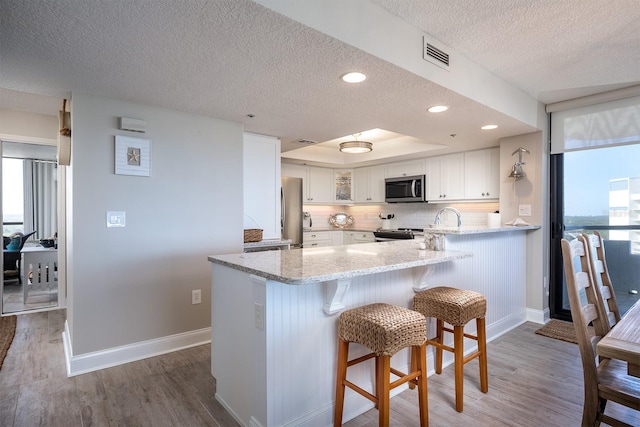 kitchen featuring kitchen peninsula, appliances with stainless steel finishes, a textured ceiling, hardwood / wood-style flooring, and white cabinetry