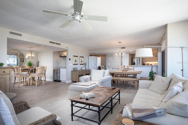 living room featuring ceiling fan with notable chandelier, light hardwood / wood-style floors, and a textured ceiling