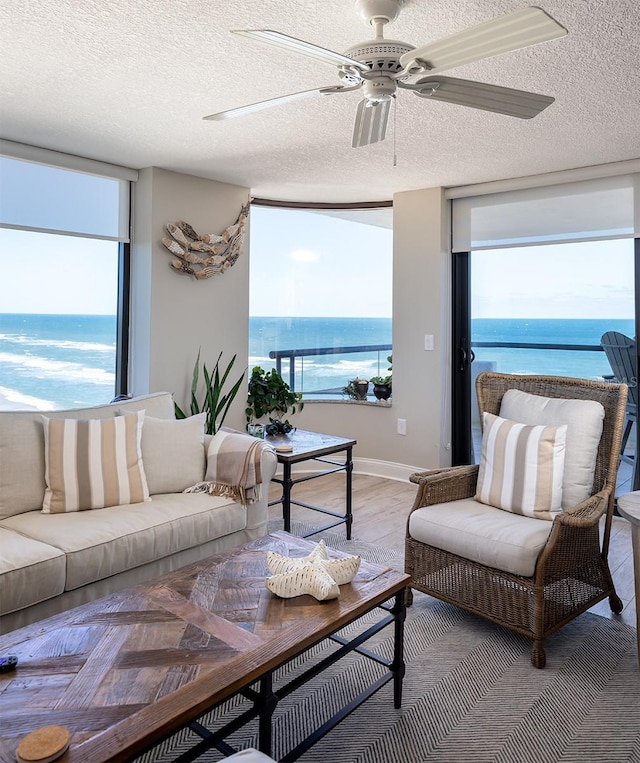 living room with a textured ceiling, a water view, ceiling fan, and light hardwood / wood-style floors