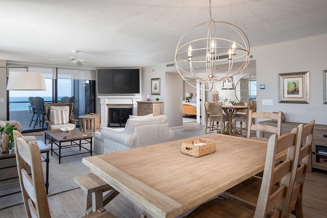 dining space with a textured ceiling, a water view, ceiling fan with notable chandelier, and hardwood / wood-style flooring