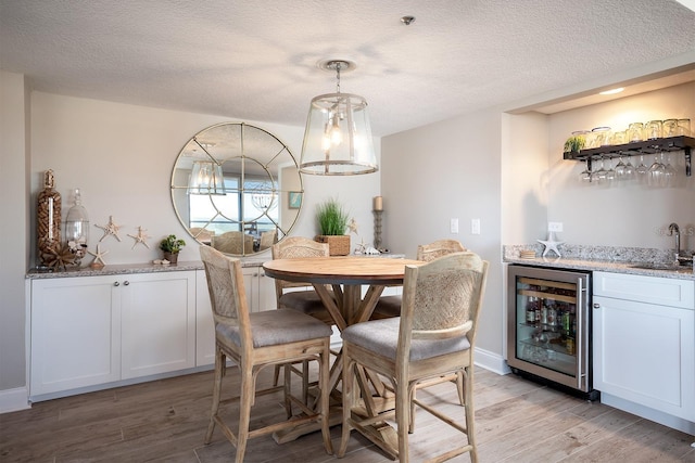 dining space with a textured ceiling, light hardwood / wood-style floors, wine cooler, and wet bar