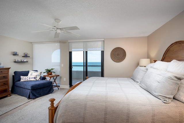 bedroom featuring access to outside, a textured ceiling, a water view, and ceiling fan