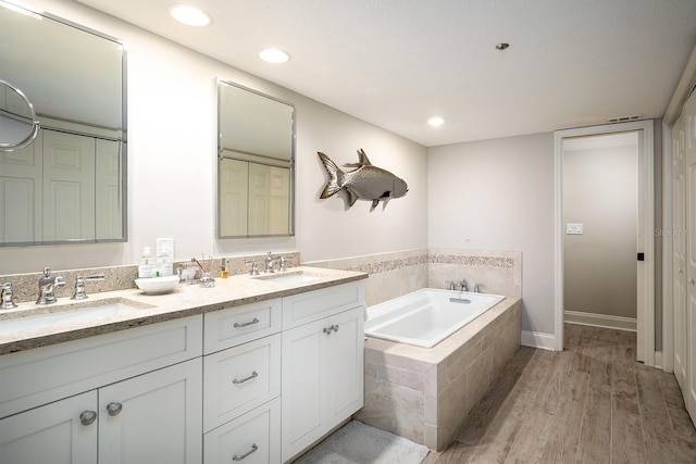 bathroom with tiled tub, hardwood / wood-style floors, and vanity