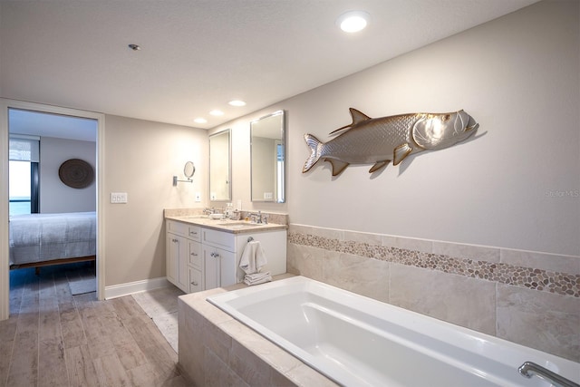 bathroom with vanity, a relaxing tiled tub, and wood-type flooring