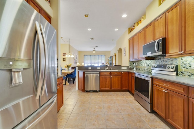 kitchen featuring sink, appliances with stainless steel finishes, hanging light fixtures, tasteful backsplash, and kitchen peninsula