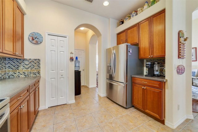 kitchen with light tile patterned flooring, stainless steel fridge, decorative backsplash, and stove