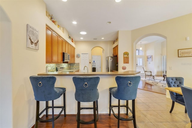 kitchen featuring a breakfast bar area, light tile patterned floors, appliances with stainless steel finishes, kitchen peninsula, and decorative backsplash