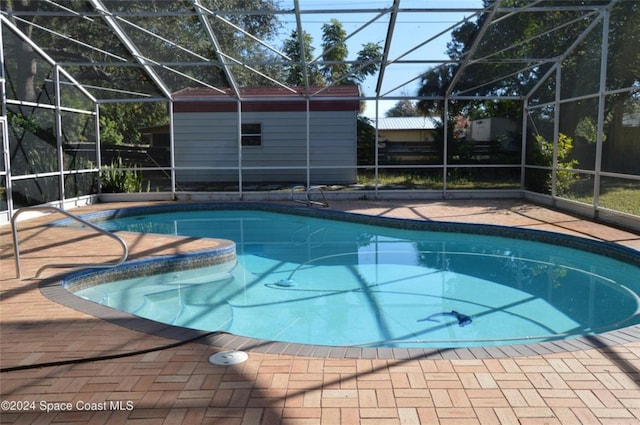 view of swimming pool with a lanai, a storage unit, and a patio area