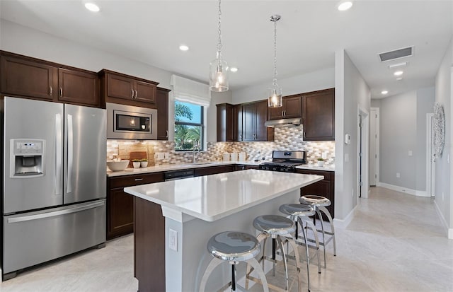 kitchen featuring a kitchen breakfast bar, backsplash, pendant lighting, a kitchen island, and appliances with stainless steel finishes