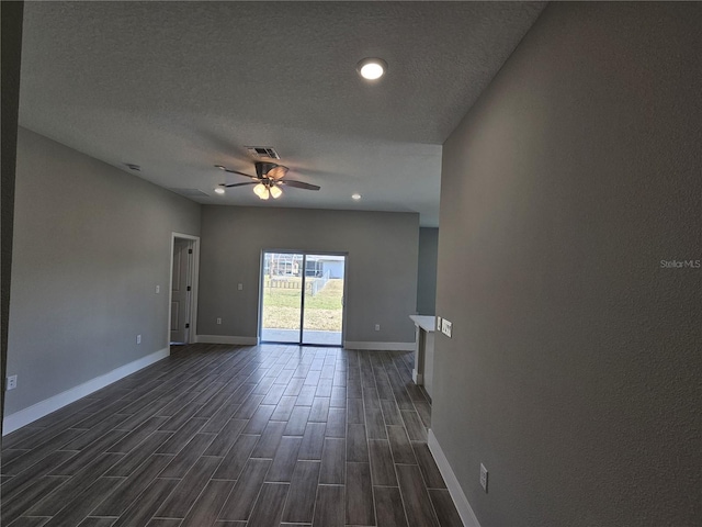 empty room featuring baseboards, visible vents, a ceiling fan, dark wood-style flooring, and a textured ceiling