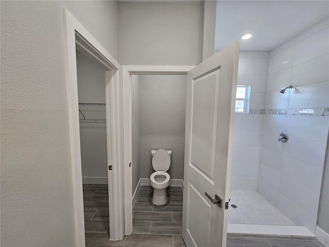 full bath with toilet, baseboards, a tile shower, wood tiled floor, and a walk in closet