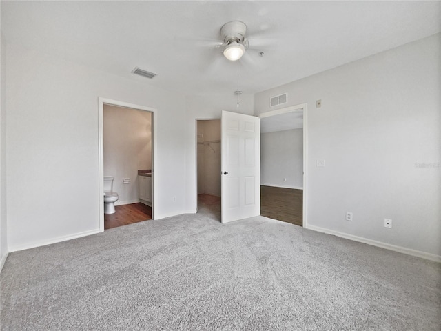 unfurnished bedroom with dark carpet, ensuite bathroom, a walk in closet, ceiling fan, and a closet