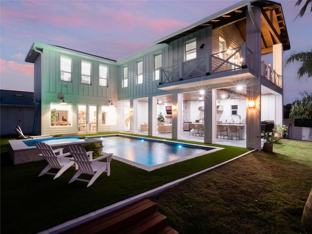 back house at dusk featuring an outdoor bar, a swimming pool with hot tub, a balcony, a yard, and a patio