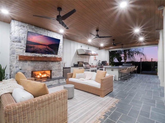 patio terrace at dusk featuring a grill, a fireplace, exterior bar, and exterior kitchen