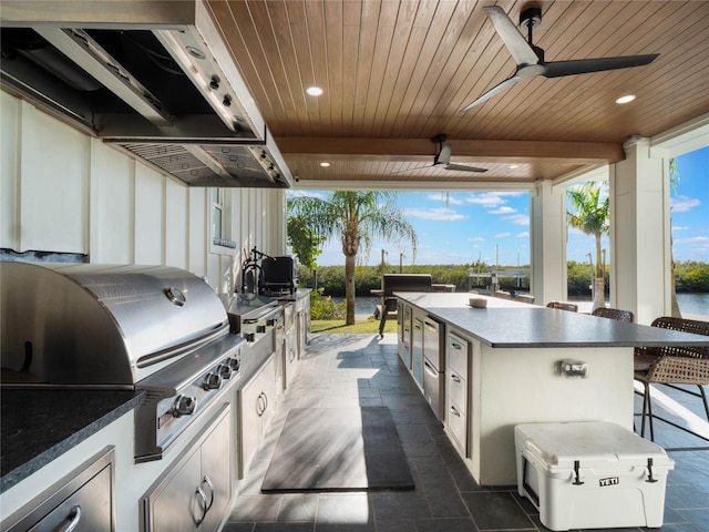 view of patio featuring ceiling fan, an outdoor kitchen, exterior bar, area for grilling, and a water view