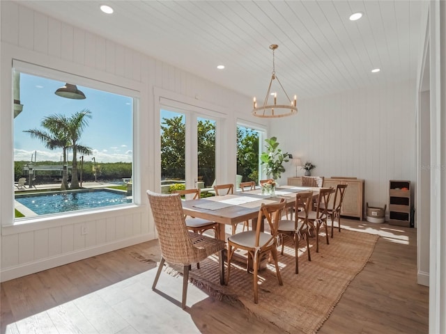 dining area featuring hardwood / wood-style floors, wood walls, and an inviting chandelier