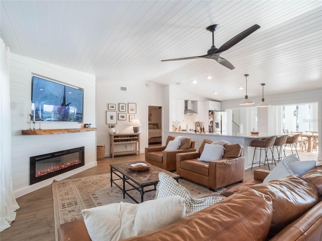 living room with hardwood / wood-style flooring, ceiling fan, a large fireplace, and wood ceiling