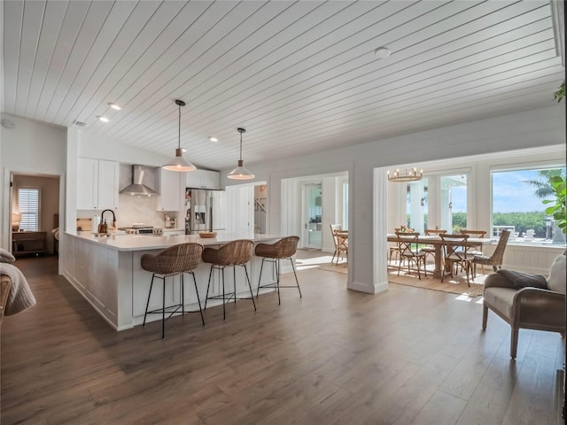 kitchen featuring dark wood-type flooring, hanging light fixtures, wall chimney range hood, stainless steel fridge with ice dispenser, and white cabinets