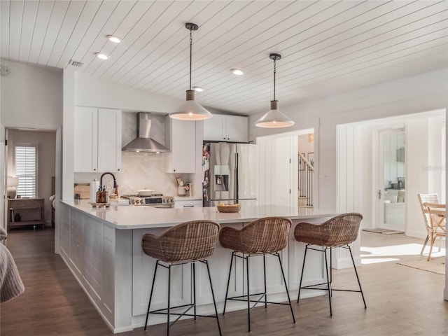 kitchen with wall chimney exhaust hood, stainless steel appliances, pendant lighting, hardwood / wood-style flooring, and white cabinets