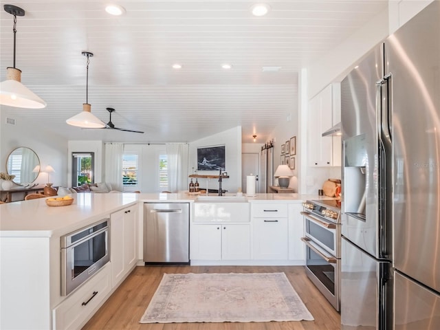 kitchen featuring appliances with stainless steel finishes, light wood-type flooring, white cabinetry, and pendant lighting