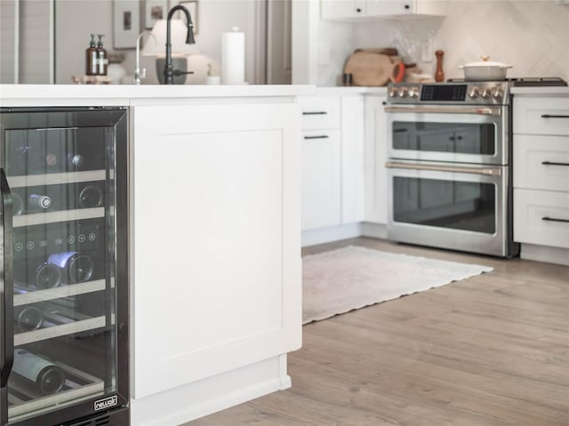 kitchen featuring white cabinets, light wood-type flooring, wine cooler, and range with two ovens