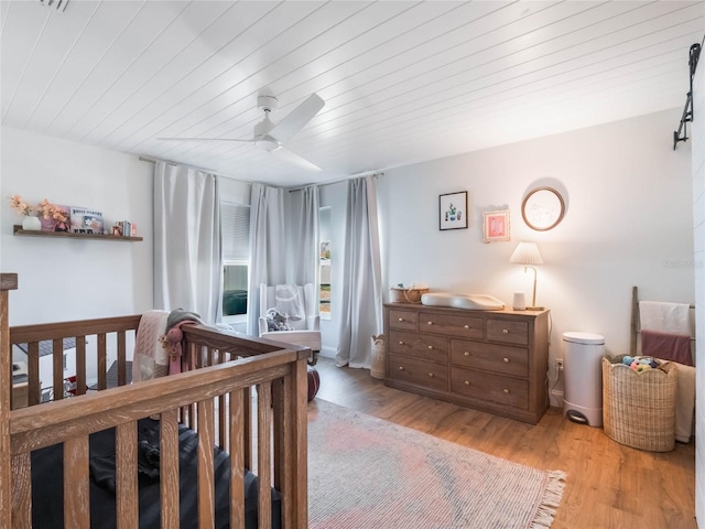 bedroom featuring a crib, light hardwood / wood-style floors, and ceiling fan