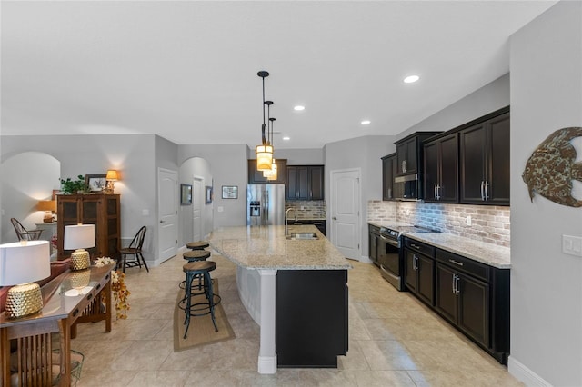 kitchen featuring light stone countertops, appliances with stainless steel finishes, backsplash, sink, and an island with sink