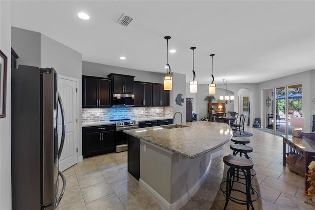 kitchen with pendant lighting, a kitchen island with sink, sink, appliances with stainless steel finishes, and a breakfast bar area