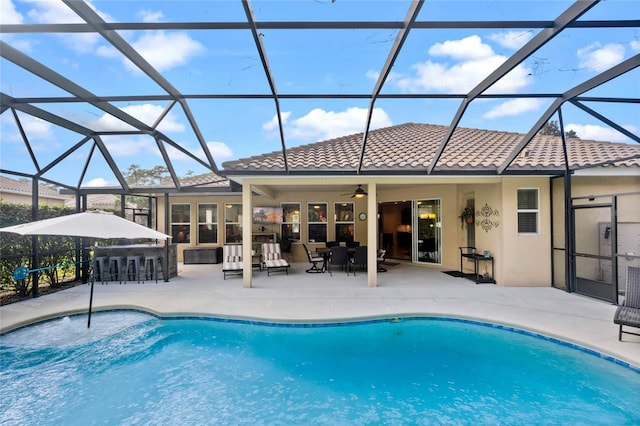 view of pool featuring glass enclosure, a bar, and a patio