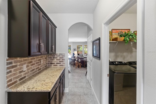 interior space with light stone countertops, tasteful backsplash, dark brown cabinets, independent washer and dryer, and light tile patterned flooring