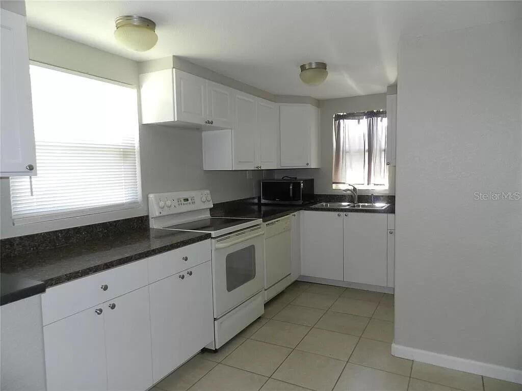 kitchen with a wealth of natural light, white cabinetry, sink, and white appliances