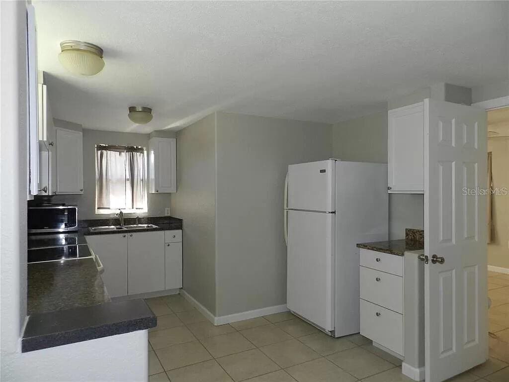 kitchen featuring light tile patterned flooring, white fridge, white cabinetry, and sink