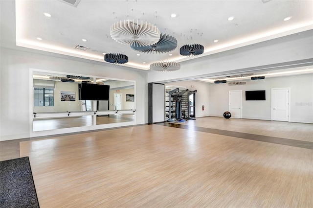 gym with light wood finished floors, a tray ceiling, visible vents, and recessed lighting