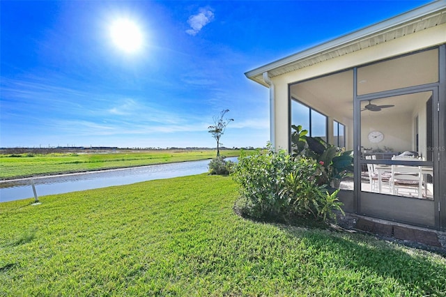 view of yard with a water view, a sunroom, and a ceiling fan