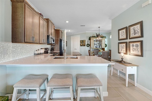 kitchen featuring appliances with stainless steel finishes, brown cabinets, a breakfast bar area, decorative light fixtures, and light countertops