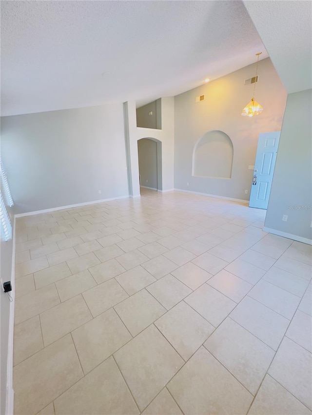 tiled empty room featuring a notable chandelier, lofted ceiling, and a textured ceiling