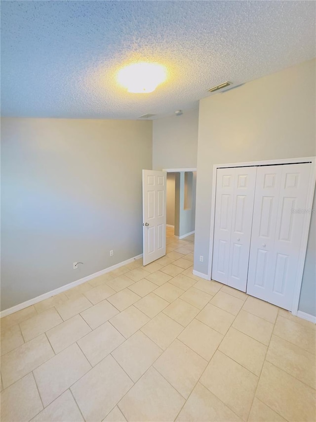 unfurnished bedroom featuring light tile patterned floors, a textured ceiling, a closet, and lofted ceiling