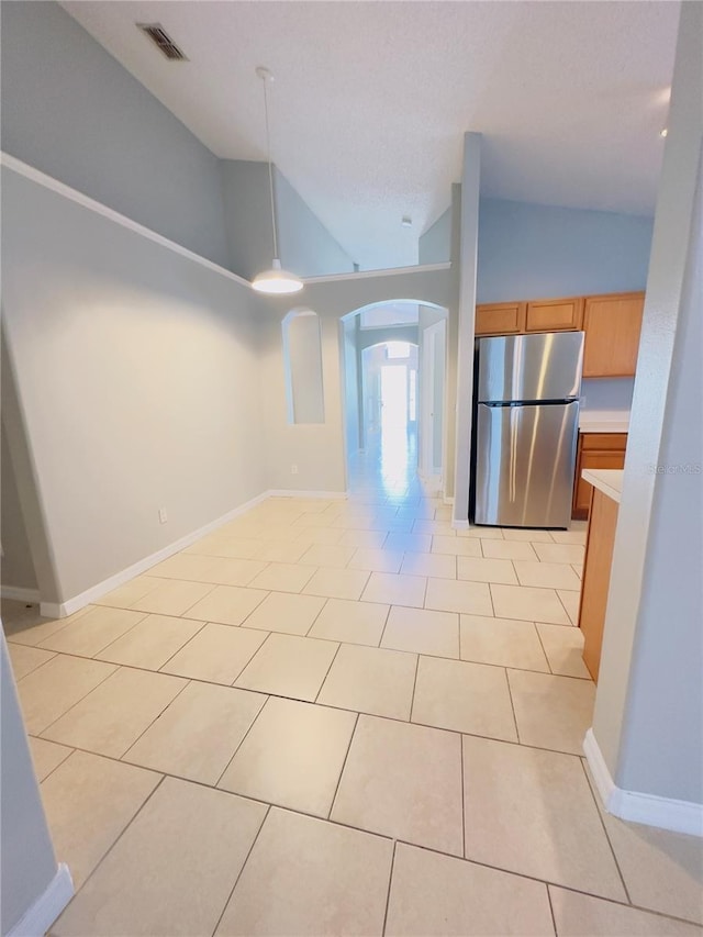 kitchen with light tile patterned flooring, stainless steel fridge, high vaulted ceiling, and hanging light fixtures