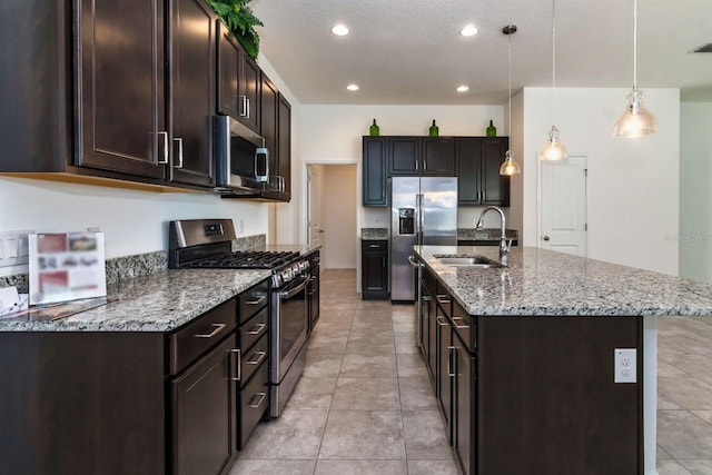 kitchen with dark brown cabinetry, sink, stainless steel appliances, decorative light fixtures, and a kitchen island with sink