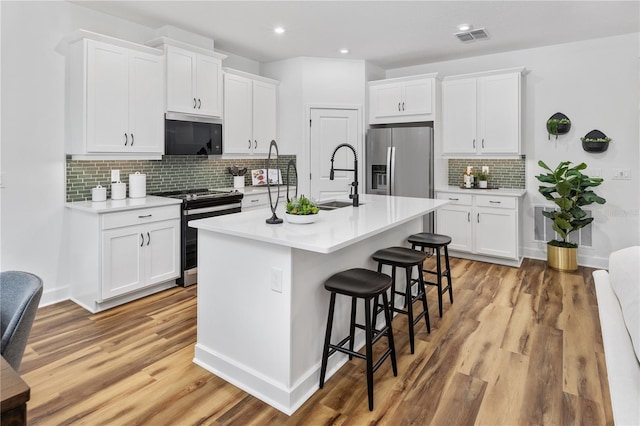 kitchen with appliances with stainless steel finishes, light wood-type flooring, white cabinetry, and a kitchen island with sink