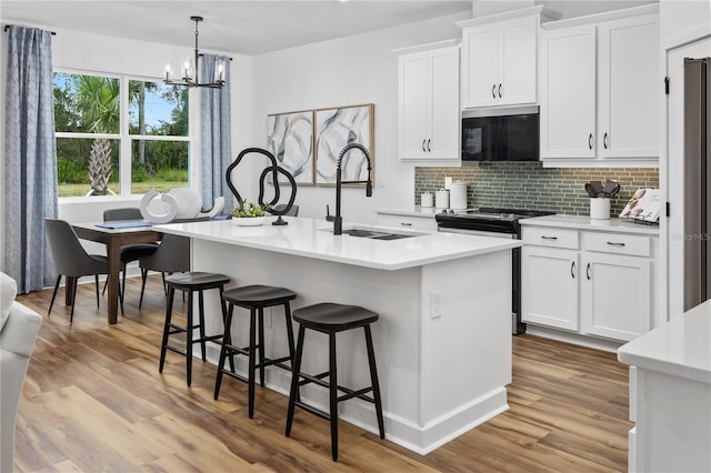 kitchen featuring appliances with stainless steel finishes, sink, a center island with sink, decorative light fixtures, and white cabinets