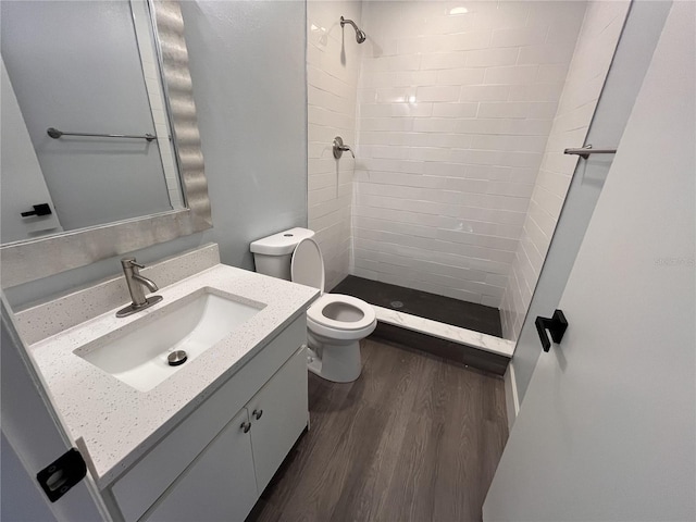 bathroom featuring tiled shower, vanity, hardwood / wood-style flooring, and toilet