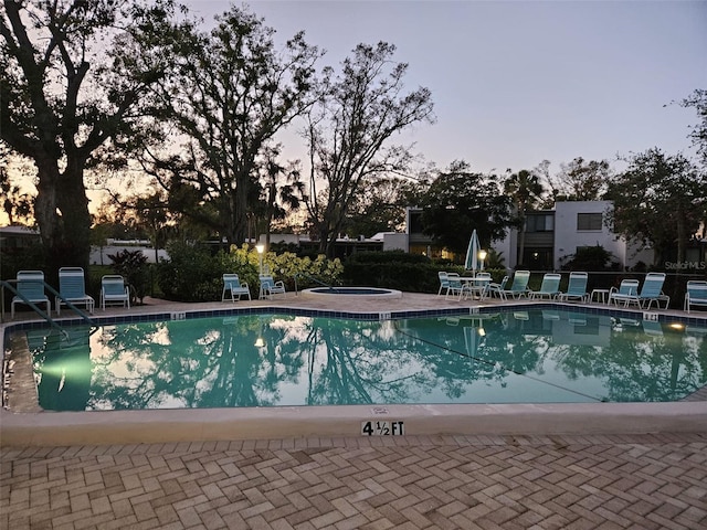 pool at dusk with a patio and a hot tub