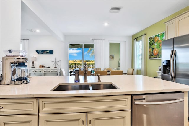 kitchen with light stone countertops, sink, stainless steel appliances, and cream cabinetry