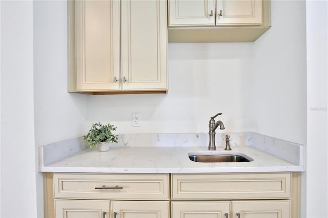 kitchen featuring light stone countertops, cream cabinets, and sink