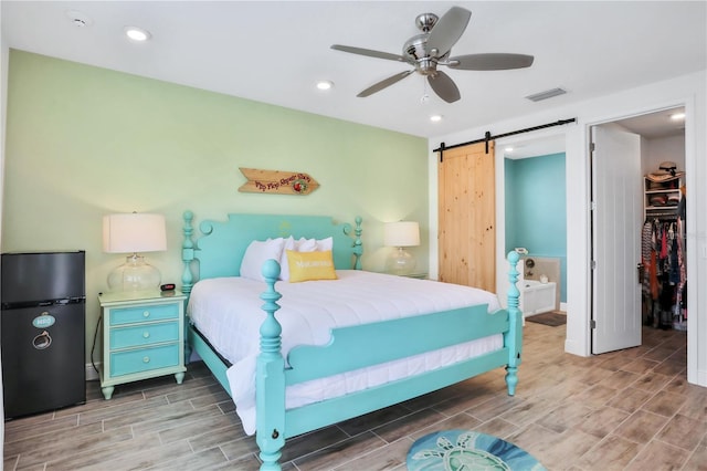 bedroom featuring ceiling fan, wood-type flooring, a barn door, a spacious closet, and a closet